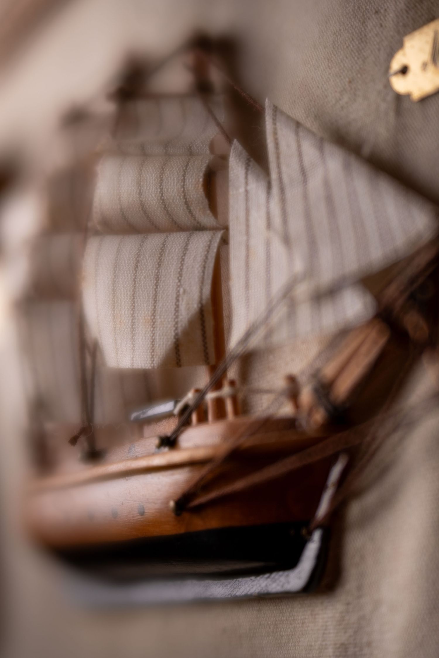 Handcrafted wooden model sailboat with fabric sails displayed on a textured beige background.