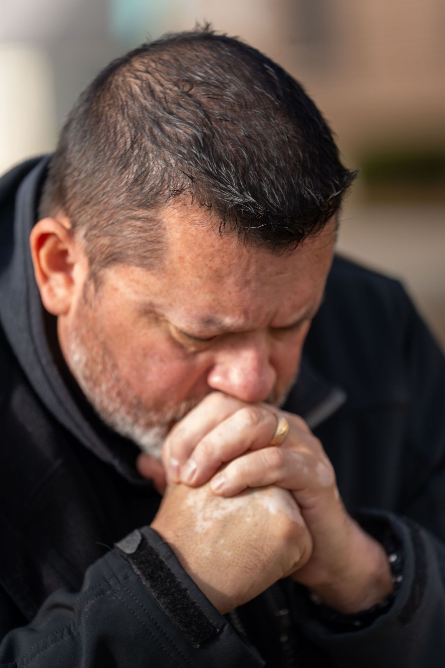 Close-up view of a person in a black hoodie covering their face with their hands in apparent distress.