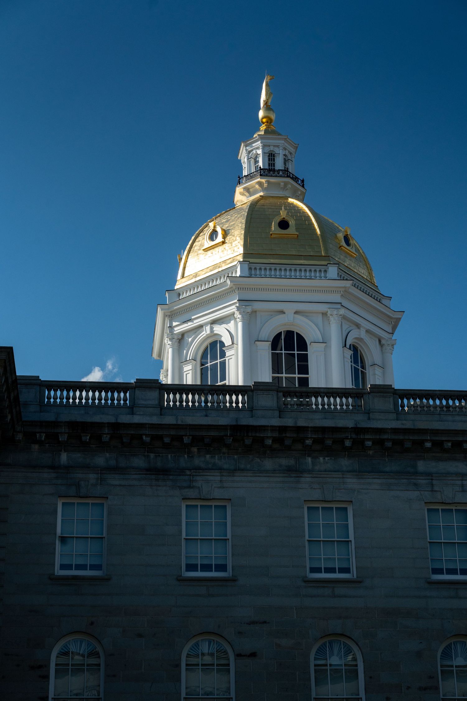 New Hampshire State Capitol building with gold dome against clear blue sky in Concord NH.