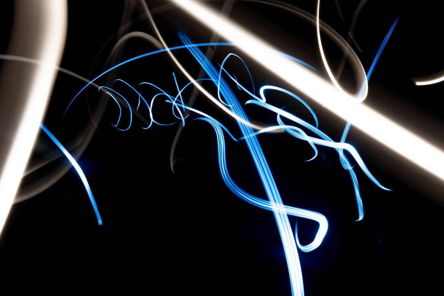 Abstract light painting photography with glowing blue and white neon streaks on a dark black background.