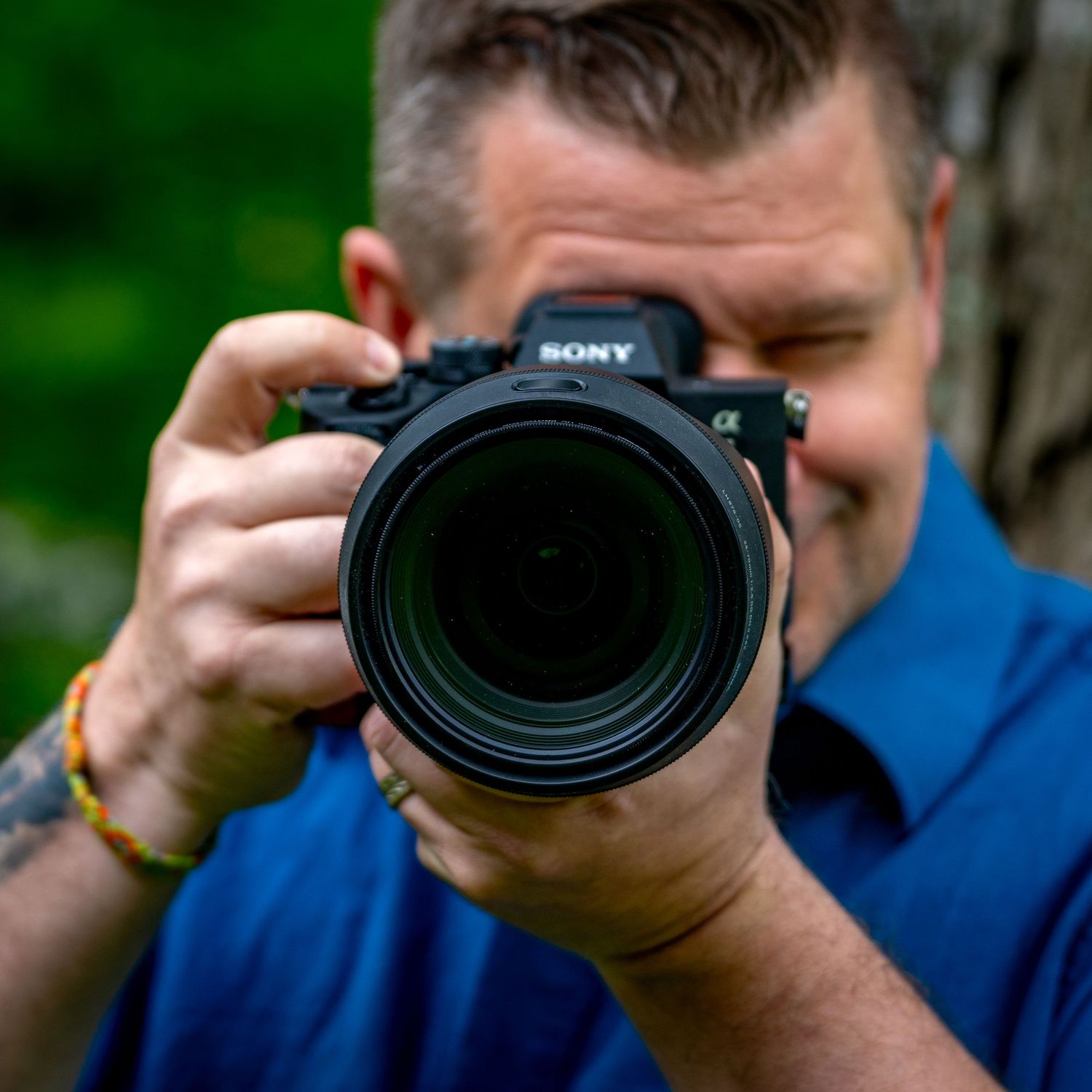 Photographer holding Sony camera with telephoto lens taking photo outdoors.