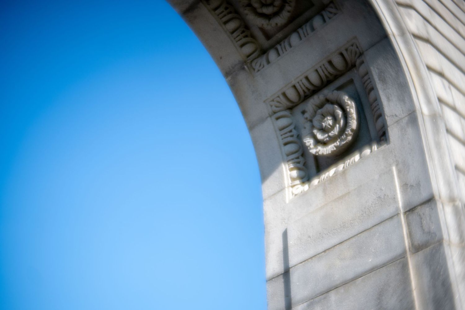 Ornate spiral volute detail on a classical stone arch against a clear blue sky.