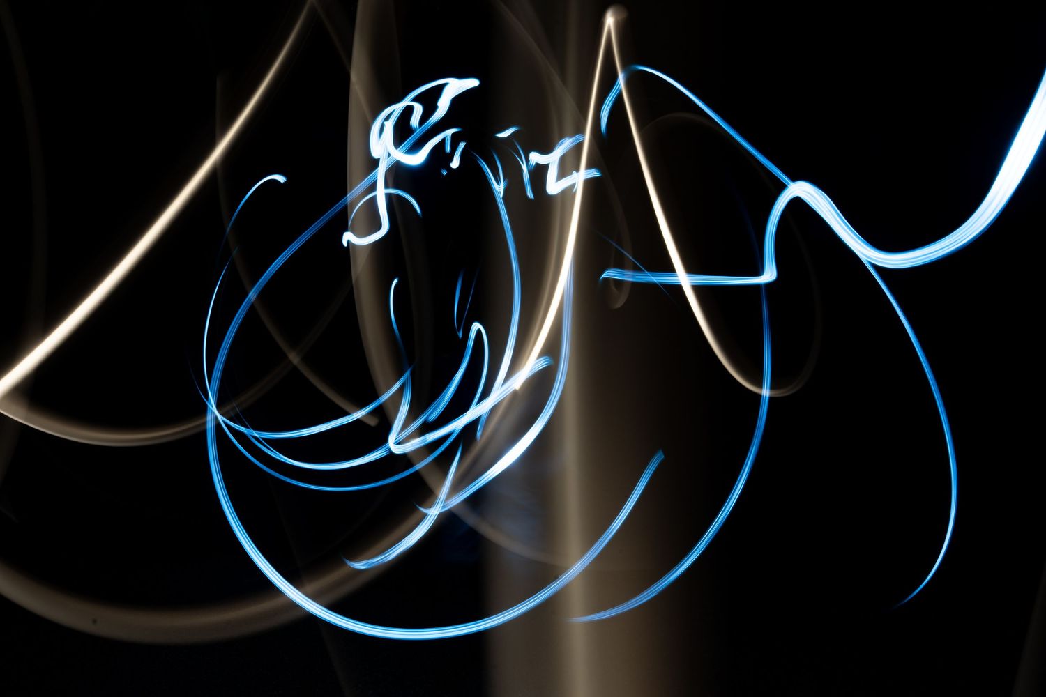 Abstract light painting with glowing blue and white streaks swirling against a dark black background.