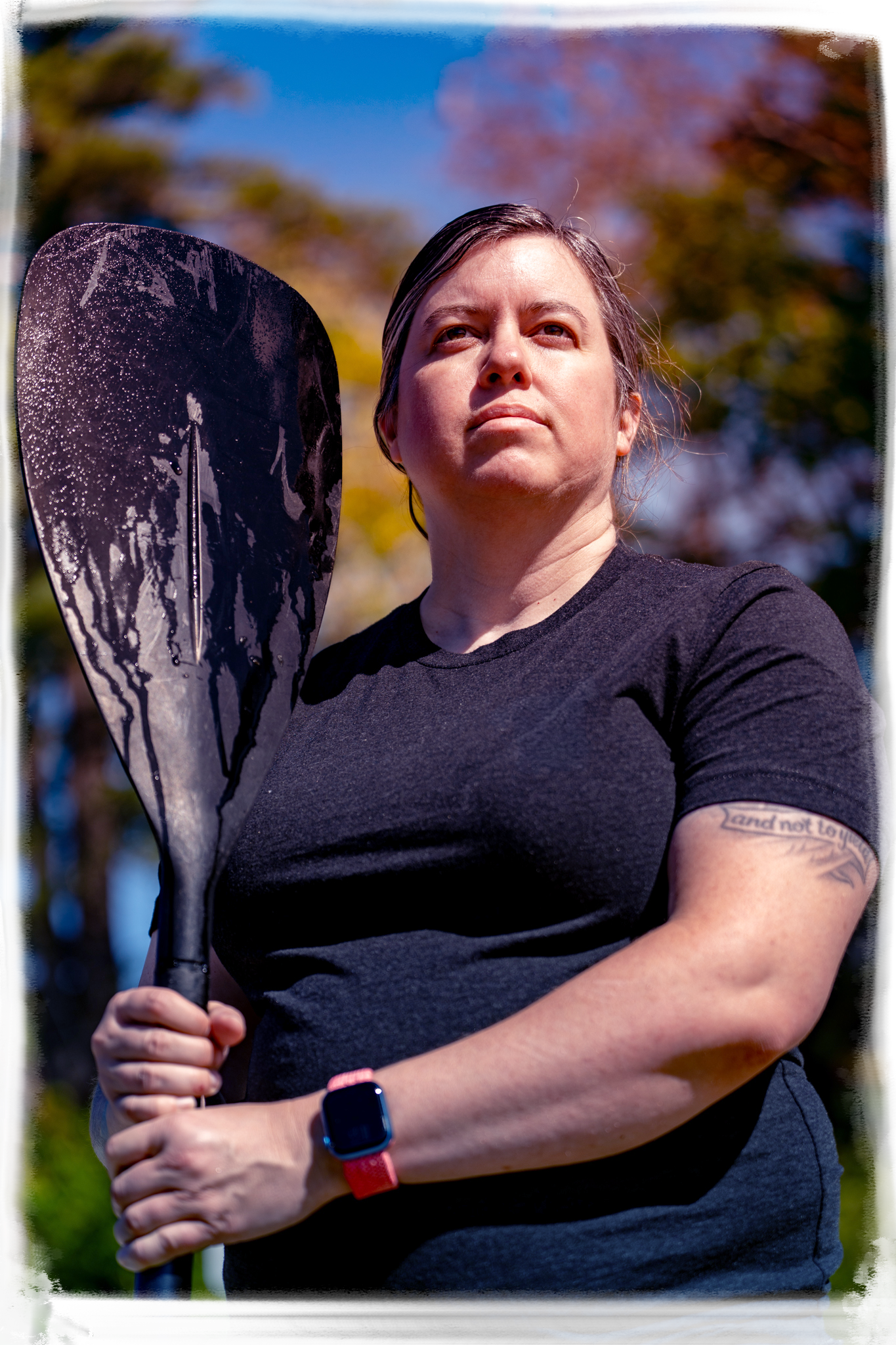 Athletic person in black t-shirt holding a paddle outdoors on a sunny day.