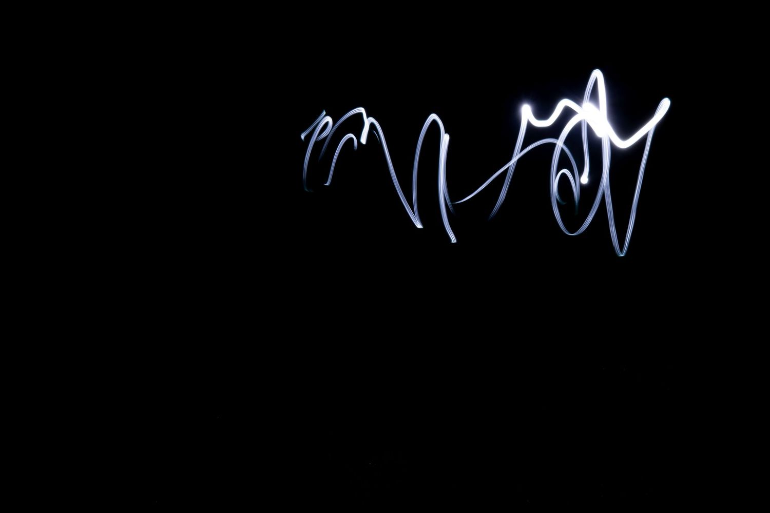 Light painting photography with glowing white cursive script against a pure black background.