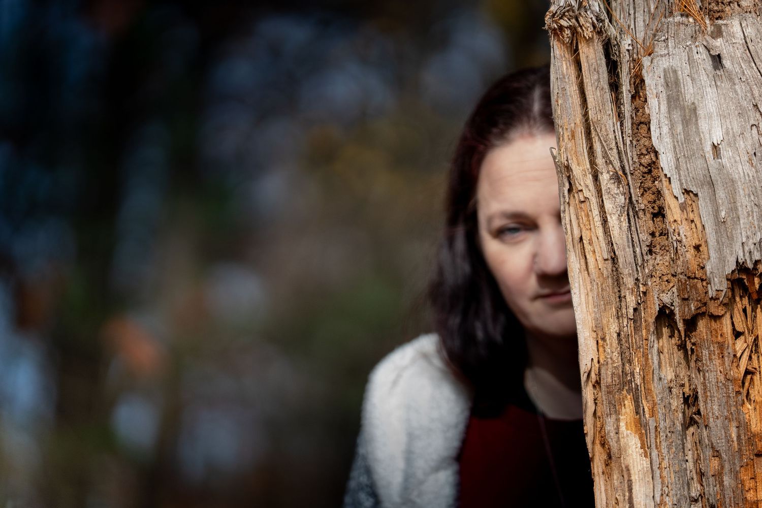 A person peeks from behind a tree trunk in an artistic outdoor portrait.