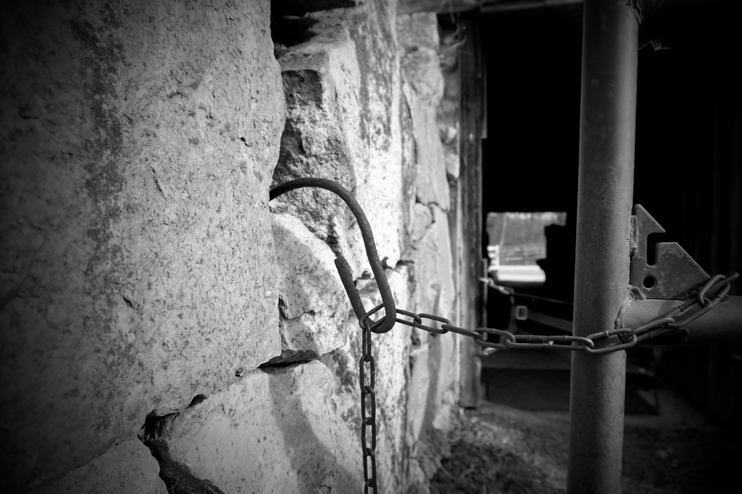 Black and white photo of a cracked concrete wall secured with a metal chain and hook.
