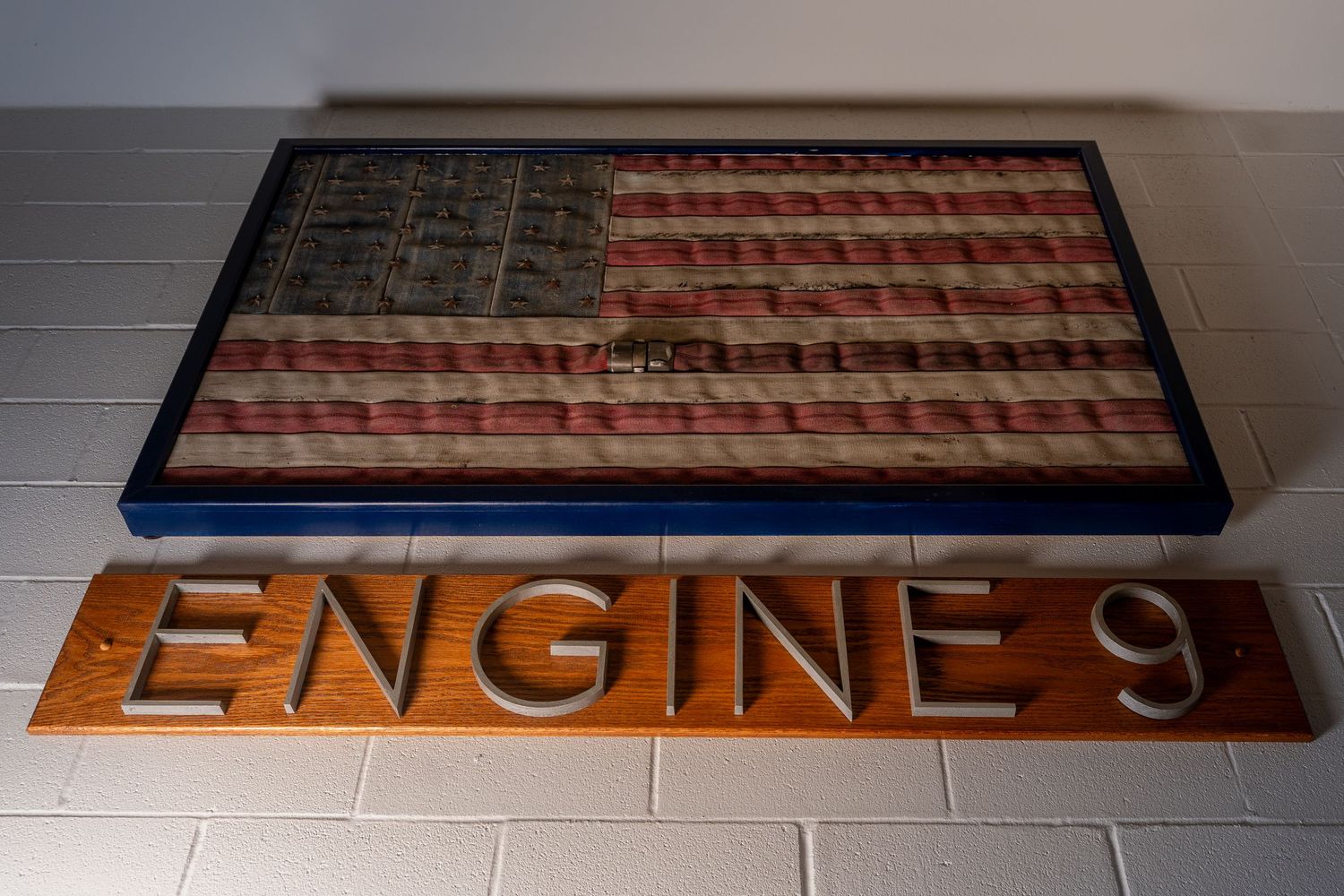 Decorative American flag artwork above an Engine 9 wooden sign mounted on a white brick wall.