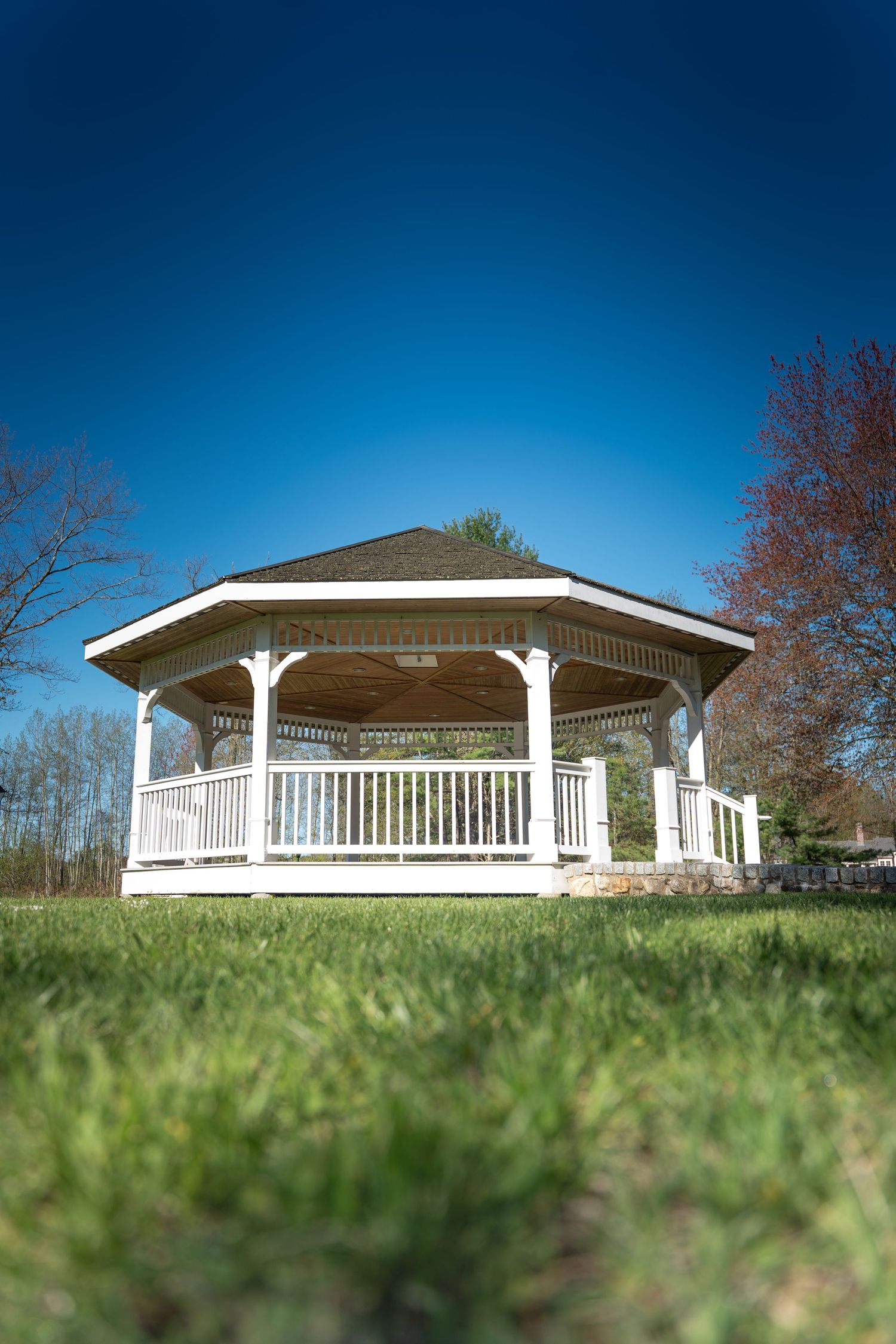 White gazebo with columns and railings on green lawn under clear blue sky.