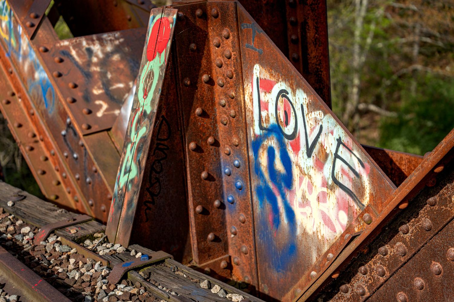 Colorful graffiti spelling LOVE on rusty riveted steel bridge beams in an outdoor setting.