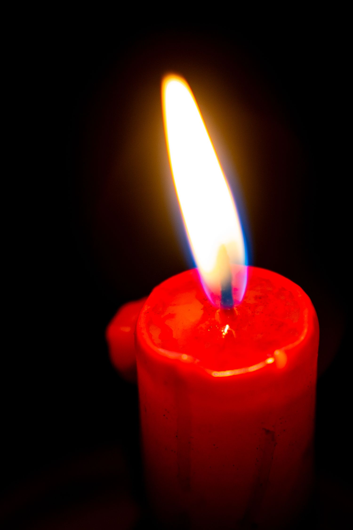 A glowing red candle with a bright flame illuminated against a dark black background.