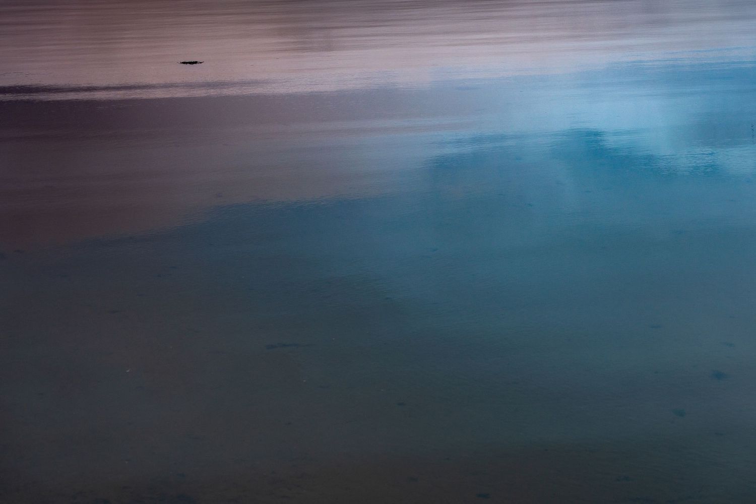 Abstract beach scene with blue sky reflections on wet sand at dusk, creating a serene coastal atmosphere.