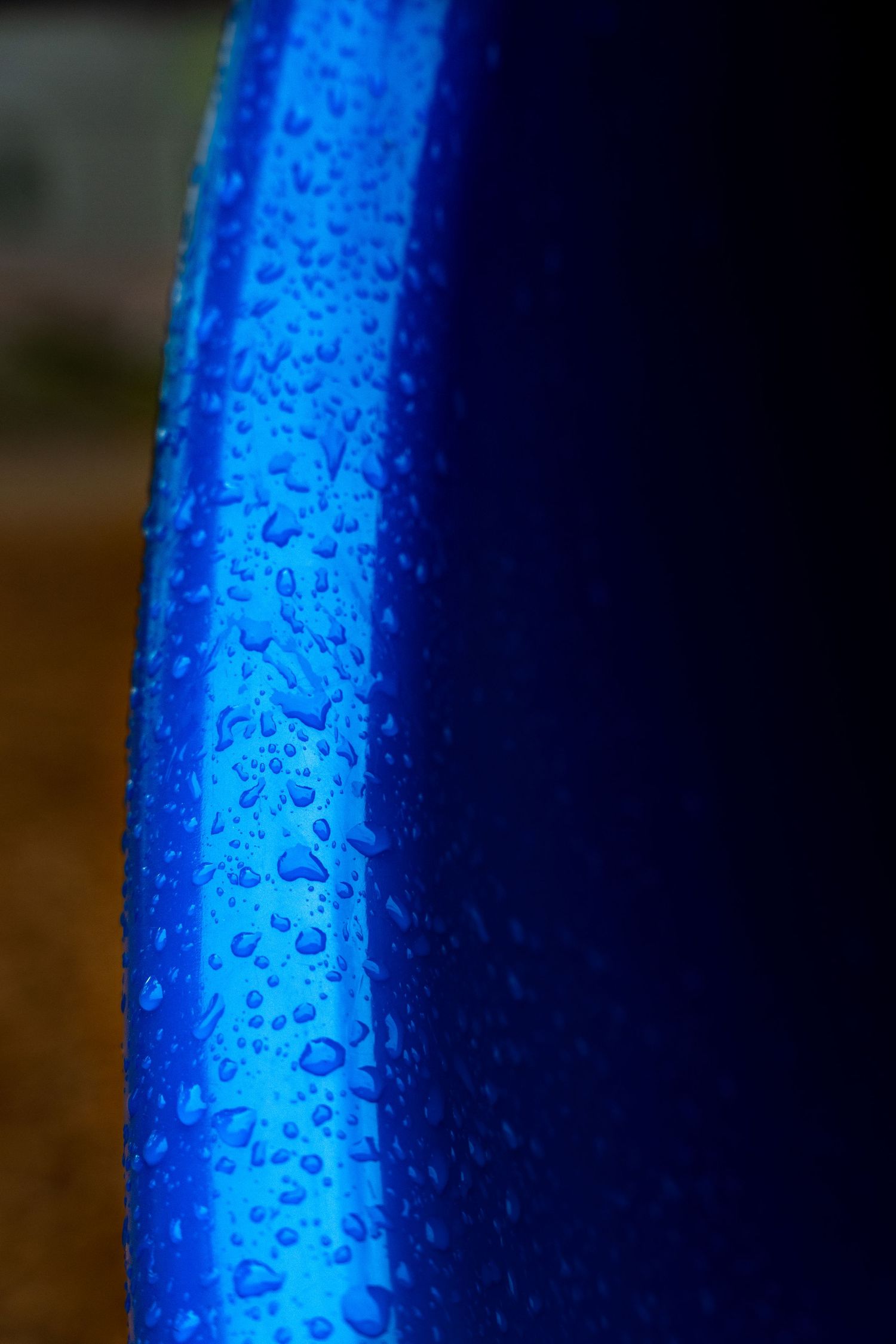 Close-up of water droplets on a curved blue surface with dark background creating a vibrant abstract pattern.