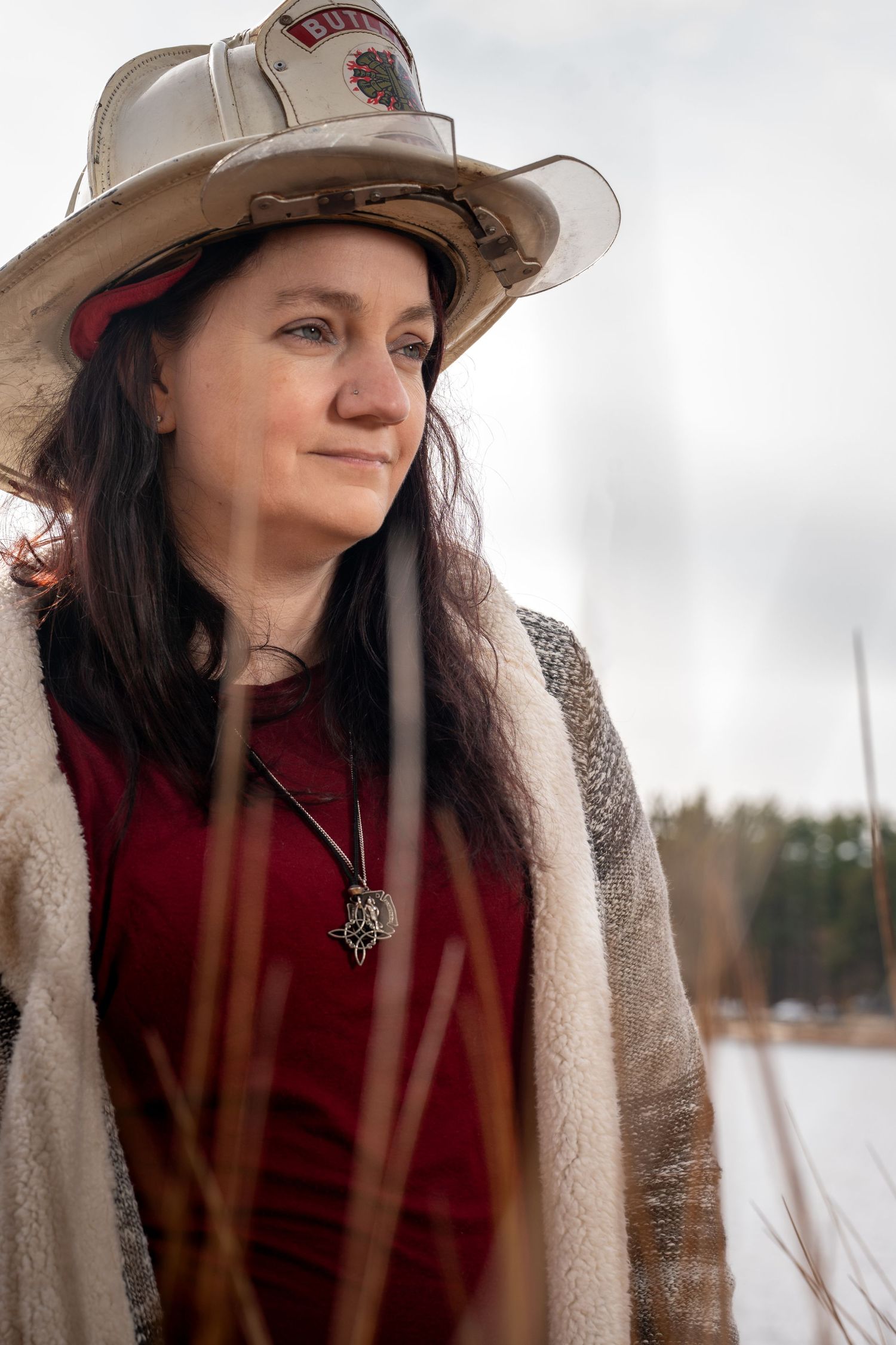 A person wearing a brown hat and cozy fleece jacket gazes thoughtfully at a winter lakeside scene.