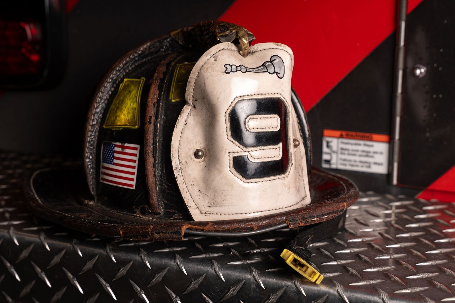 White firefighter helmet with number 9 and American flag patch resting on diamond plate surface.