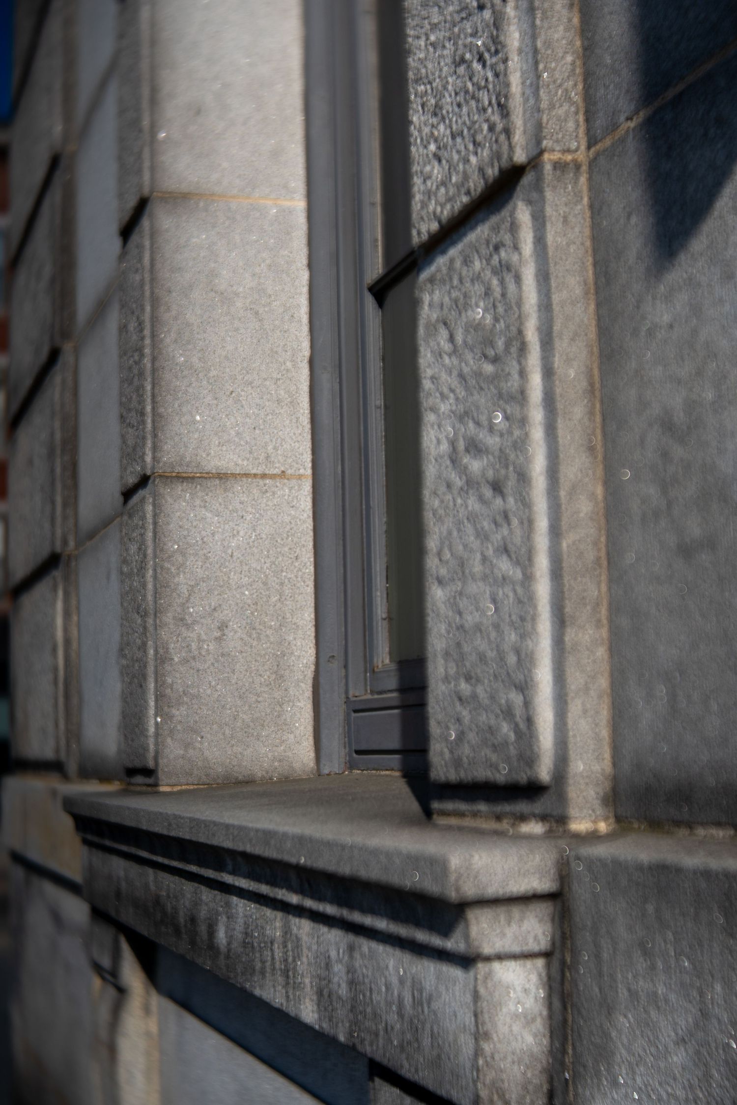 Close-up of a classic stone building facade with granite blocks, decorative molding, and a narrow dark window frame.