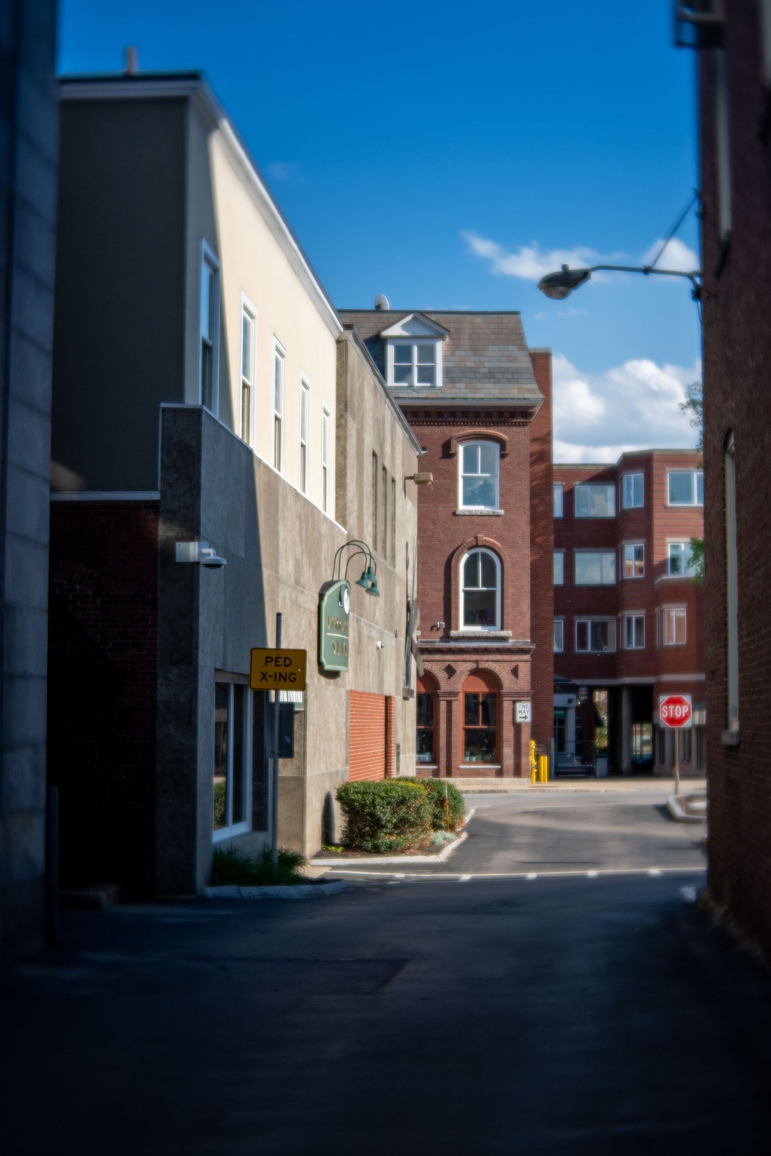 Narrow urban alley with historic brick buildings and stop sign under partly cloudy sky.