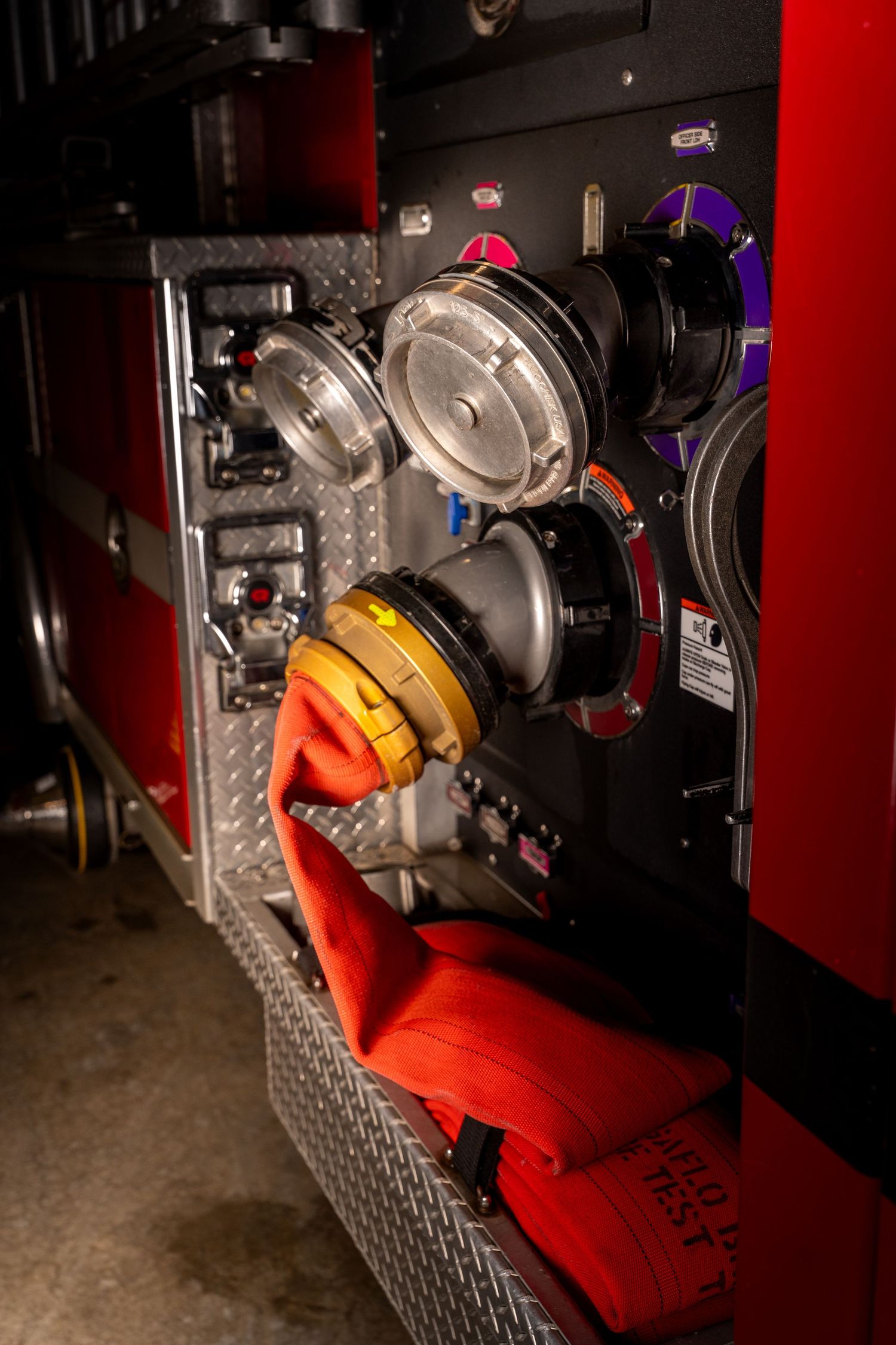 Red fire truck panel with water hose connections, gauges, and equipment compartments.