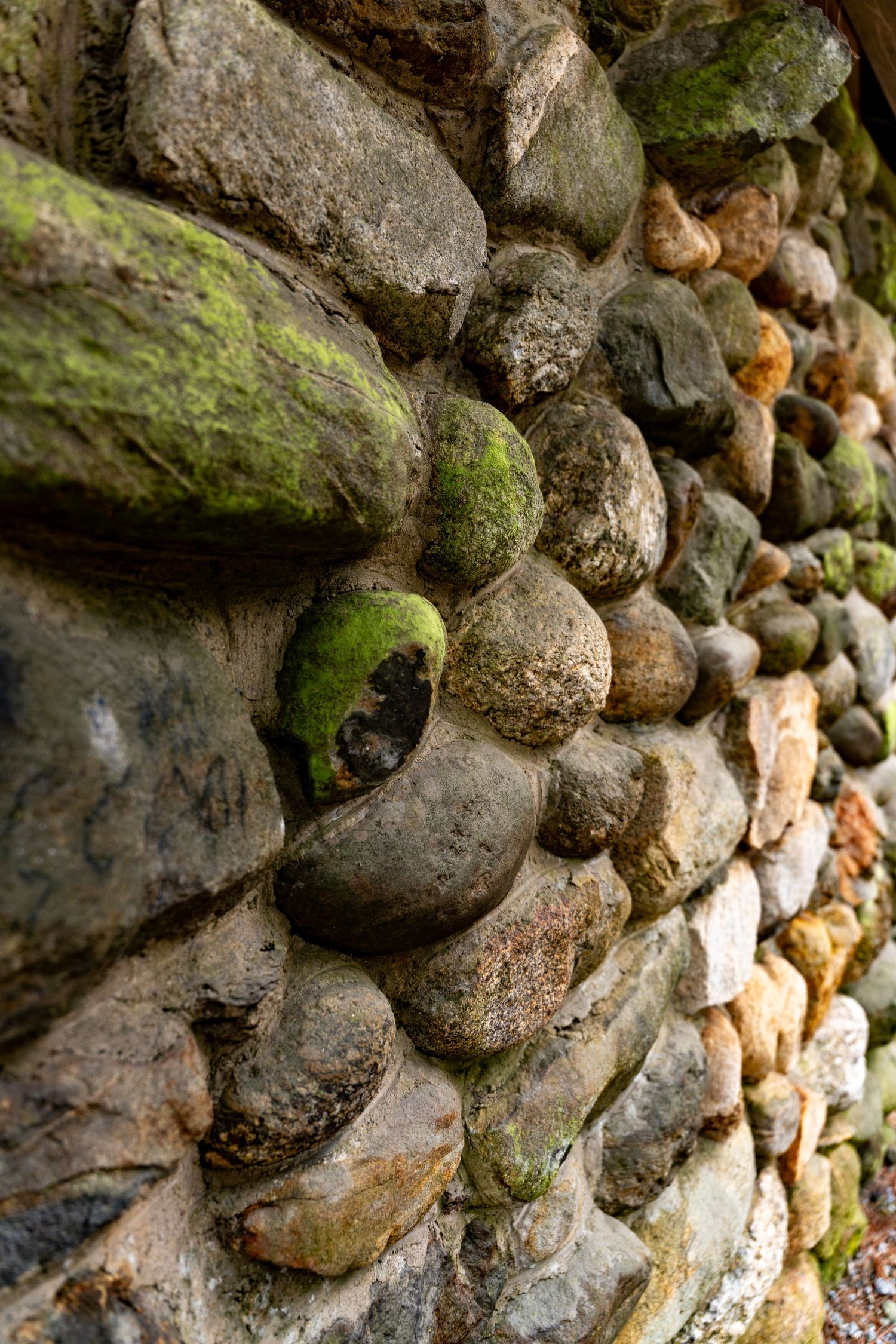 A rustic stone wall built with rounded cobblestones, some covered in green moss, photographed at an angle.