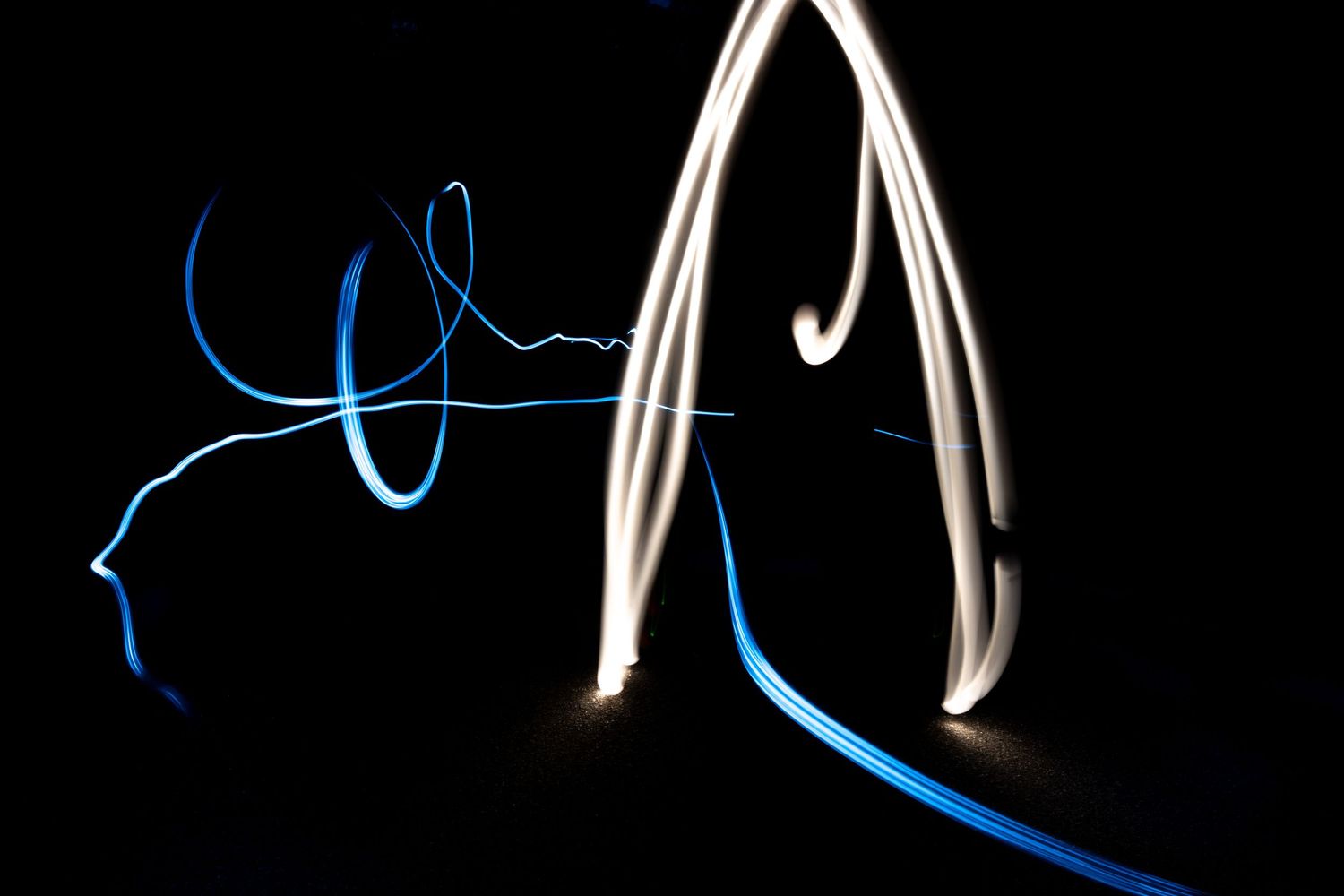 Abstract long exposure light painting with glowing white arches and blue streaks on a dark background.