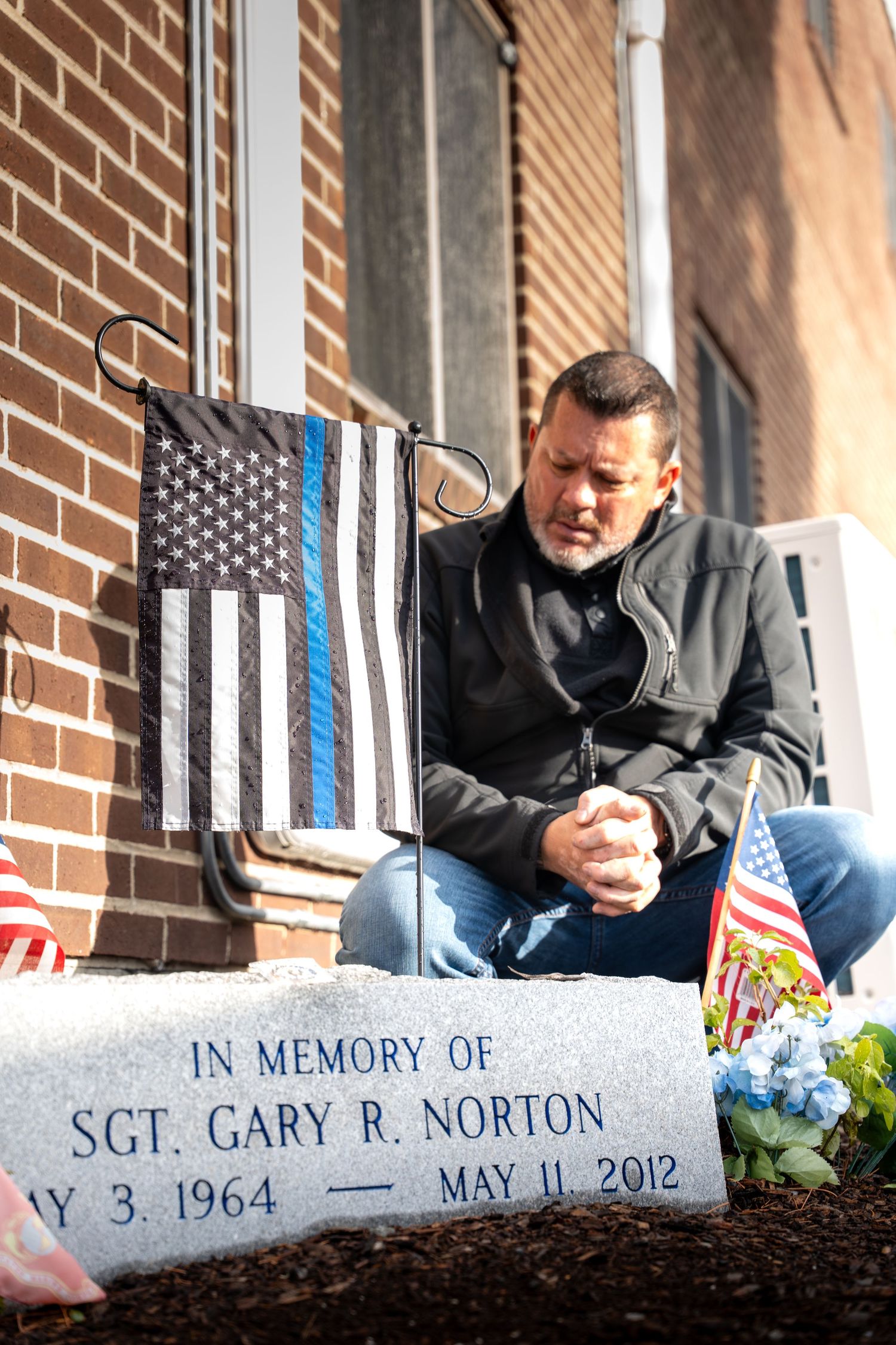 Someone pays respects at a memorial for fallen police officer Sgt. Gary R. Norton with a thin blue line flag displayed.