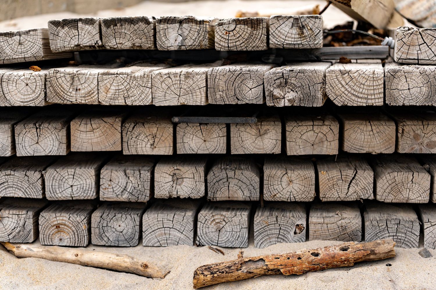 Stacked weathered gray wooden lumber planks showing tree rings on ends, arranged in neat rows outdoors.