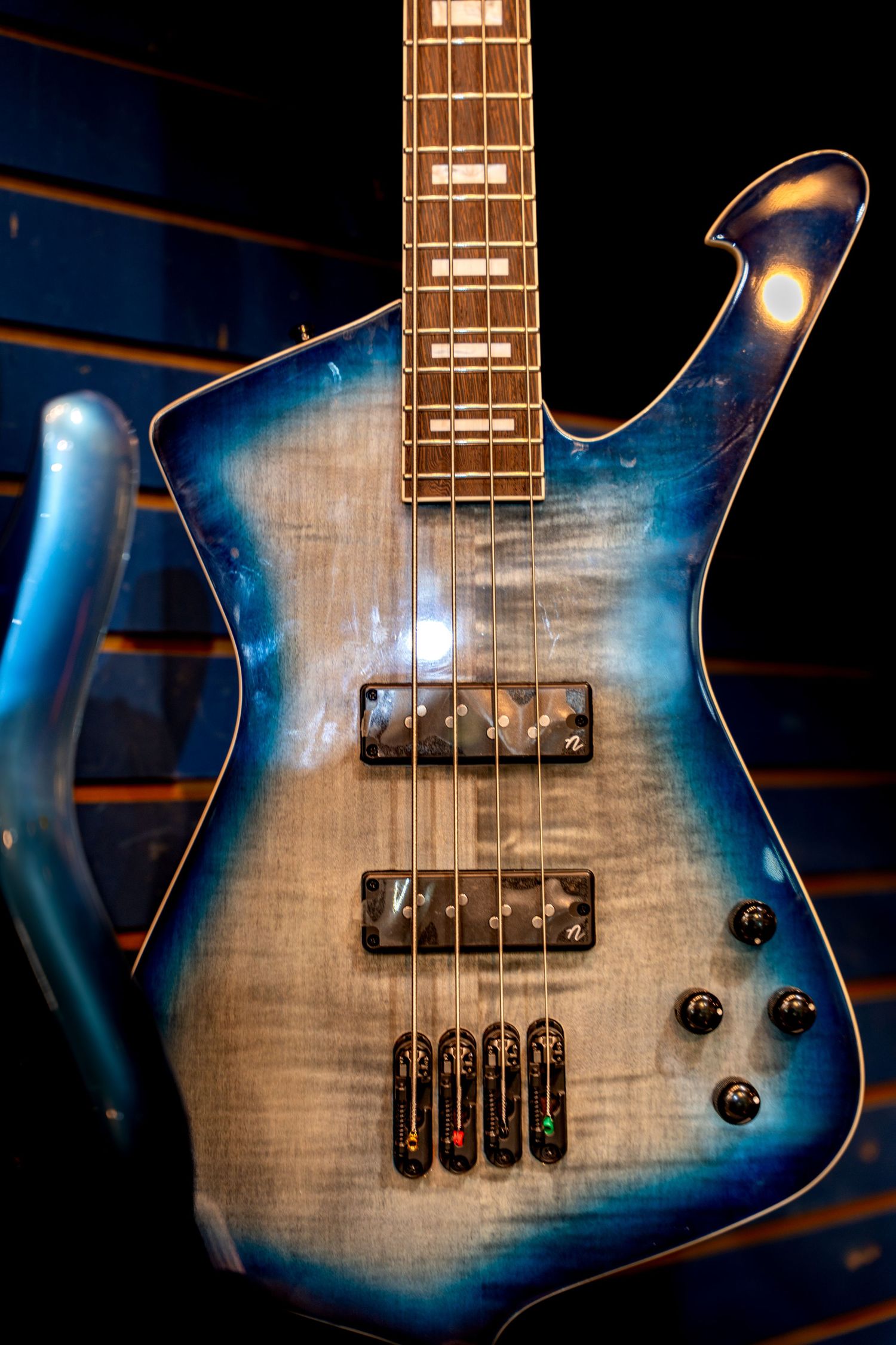 Blue flame maple bass guitar with dual humbuckers and rosewood fretboard displayed against dark background.