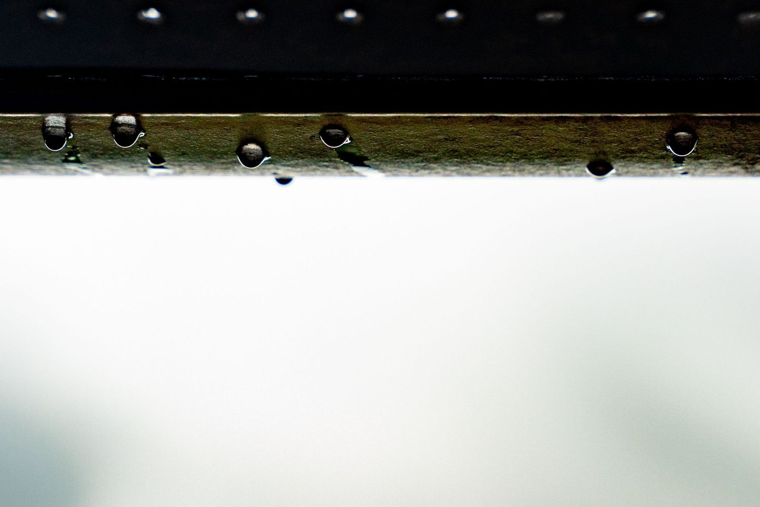 Close-up of water droplets hanging from a wooden beam against a bright white background.