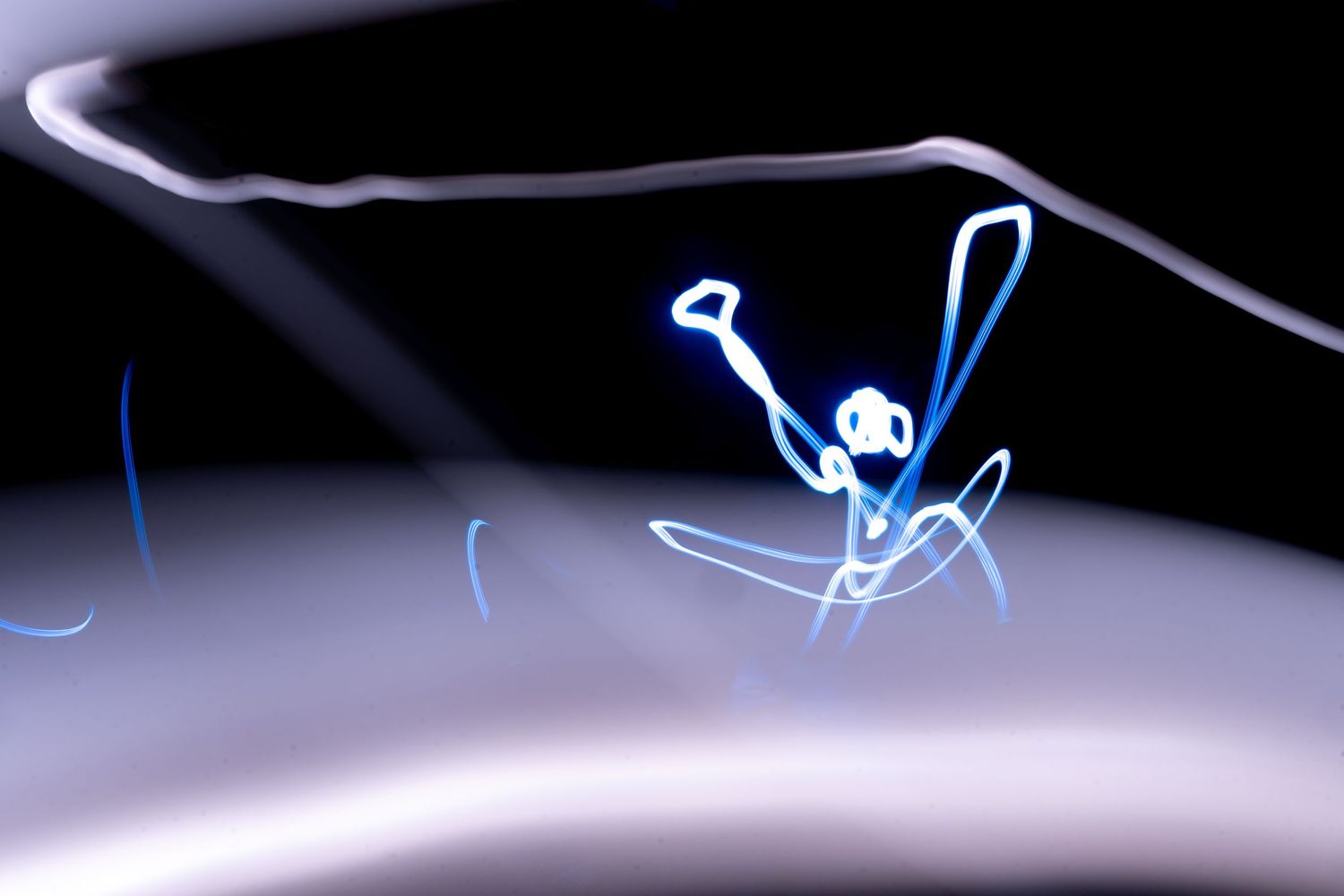 Light painting art showing a glowing blue stick figure against a dark background with white light trails.