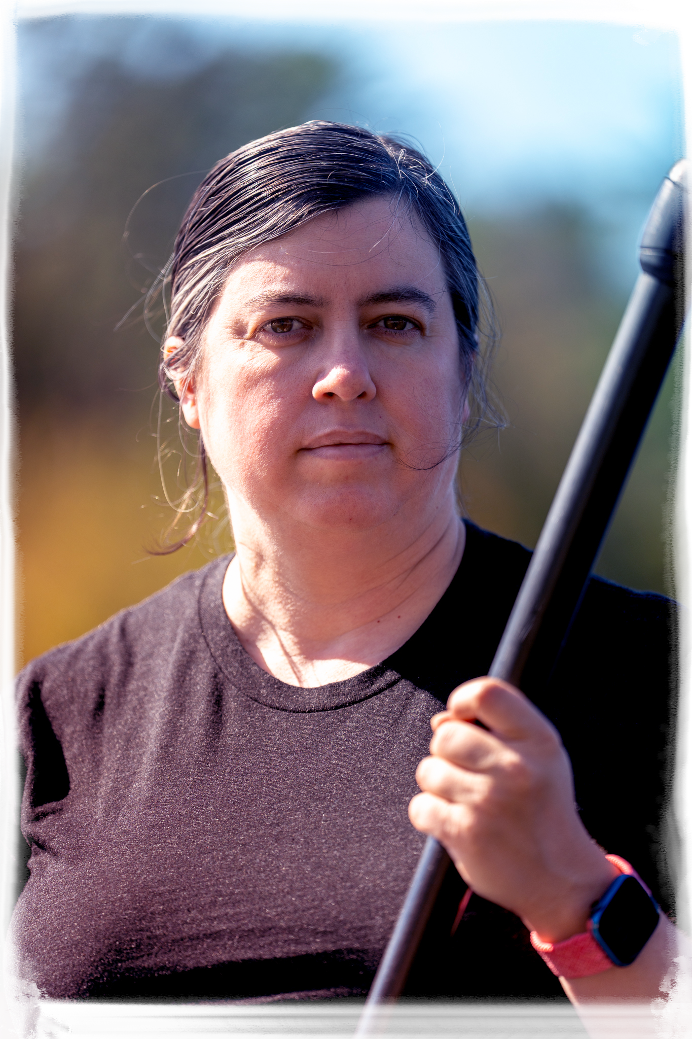Portrait of someone in a brown t-shirt holding a paddle against a blurred outdoor background.
