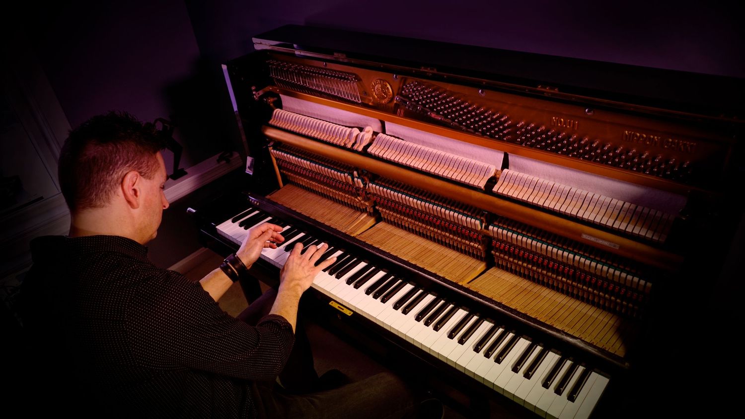 Close-up view of piano keys and interior strings illuminated by dramatic red and purple lighting.