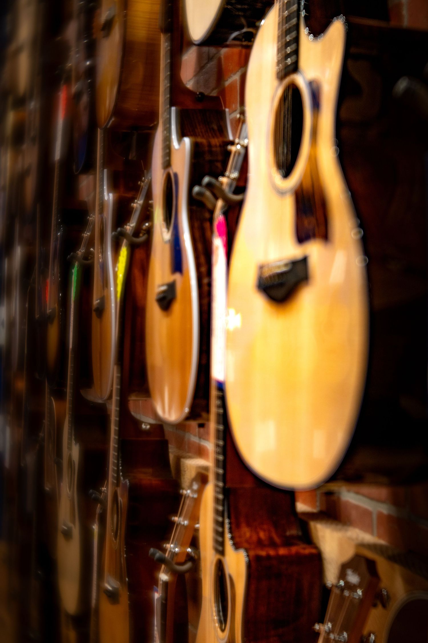 Row of acoustic guitars hanging on a brick wall display in a music store with warm lighting.
