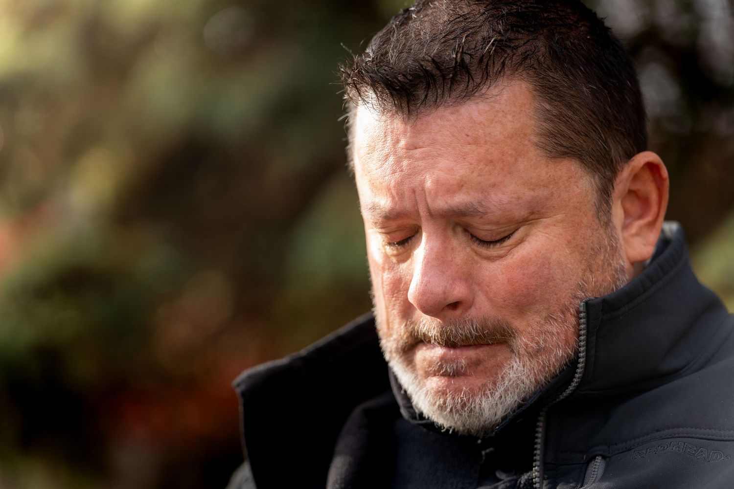 Side profile of a bearded man in black jacket showing emotional expression.