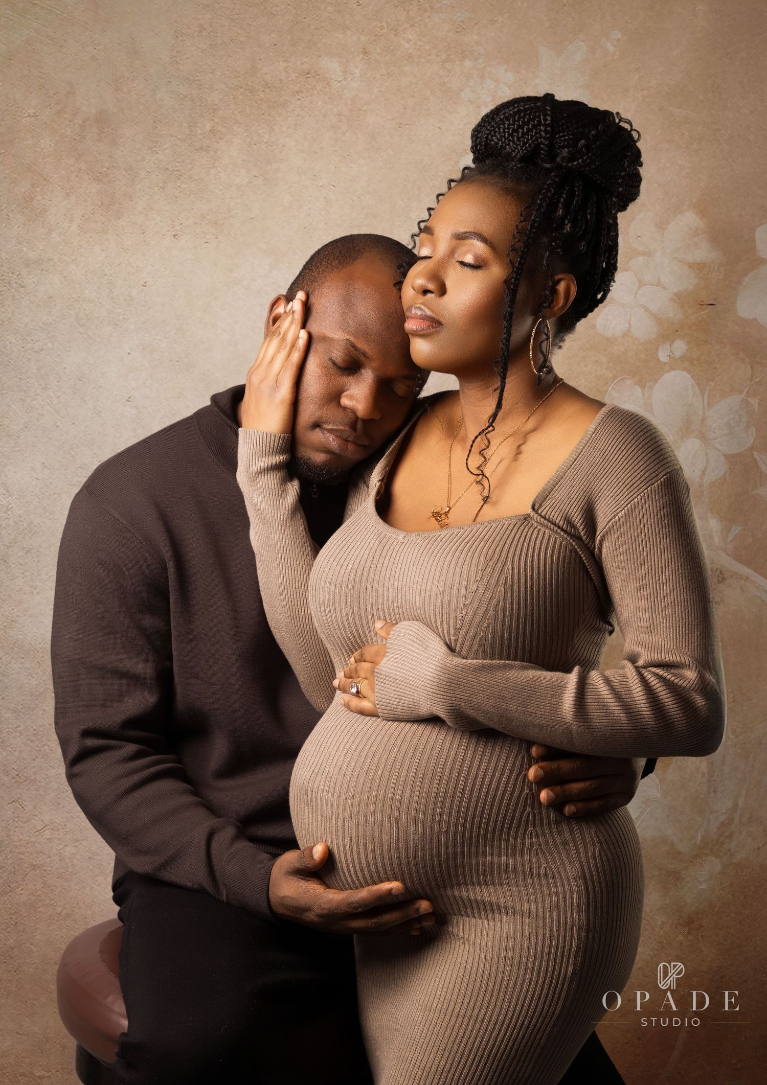 Maternity portrait of a couple, with the man gently holding the pregnant woman’s belly in an intimate studio setting.