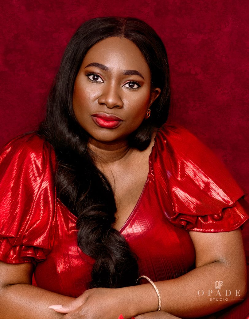 Close-up portrait of a woman in a shiny red outfit with bold makeup against a deep red background.
