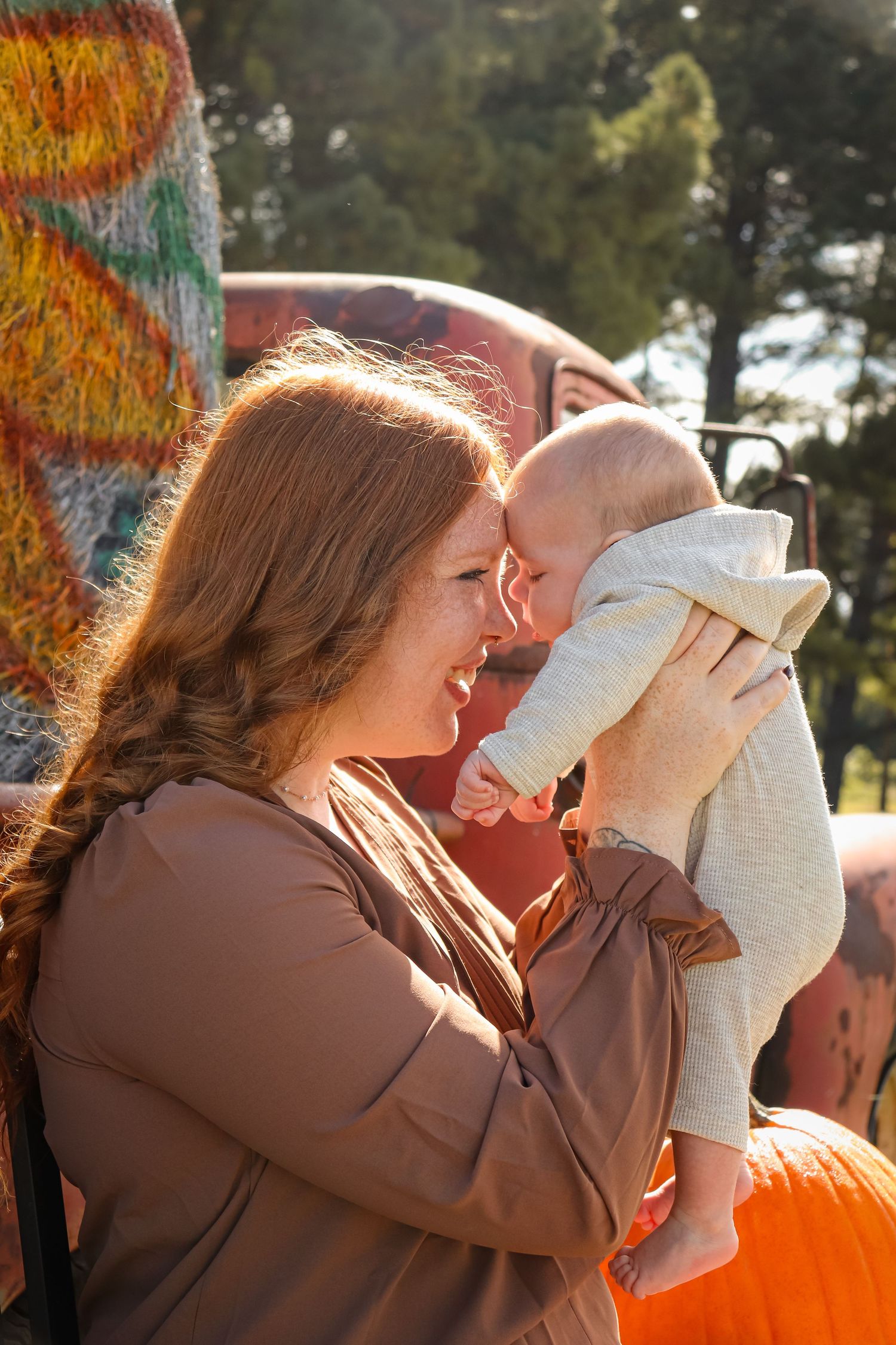 Lifestyle family session at a pumpkin patch with a mother and her baby taken outdoors in natural light, candid photography style.
