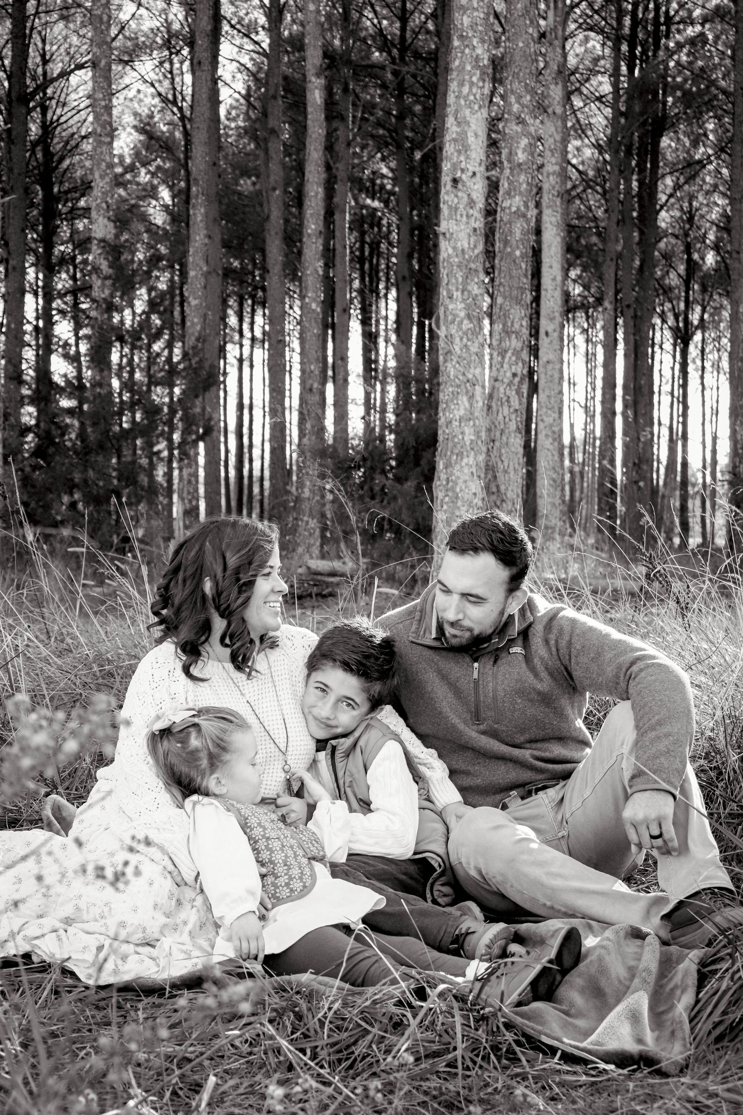Lifestyle family session with four people taken outdoors in black and white, candid photography style.