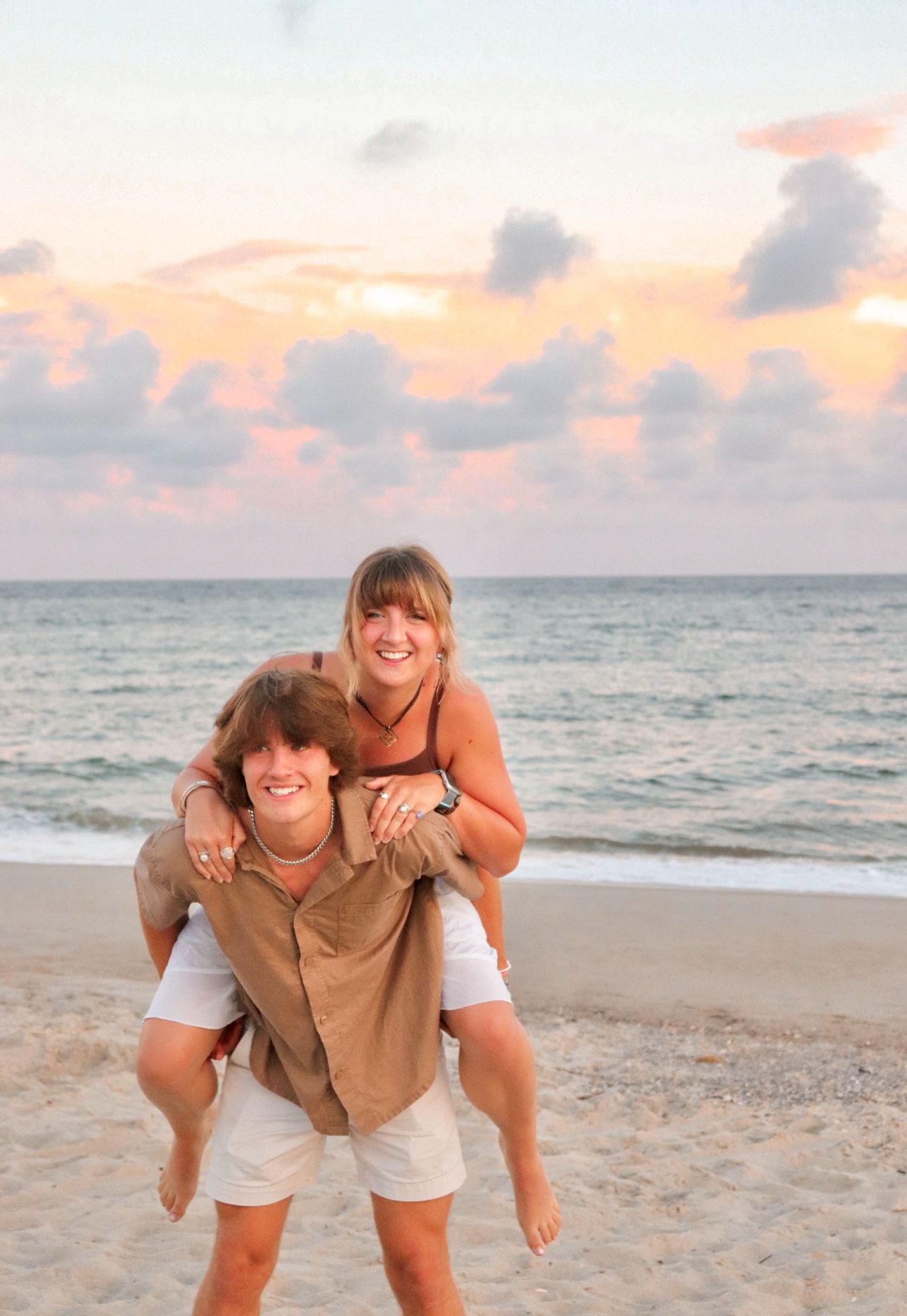 Lifestyle family session with two sibling on each others backs out on the beach, taken outdoors in natural light, candid photography style.