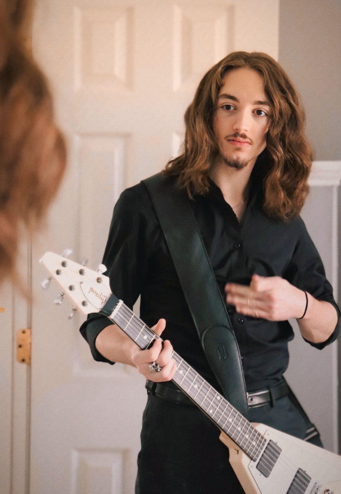 candid portrait of a man adjusting his guitar strap, taken indoors in a light atmosphere