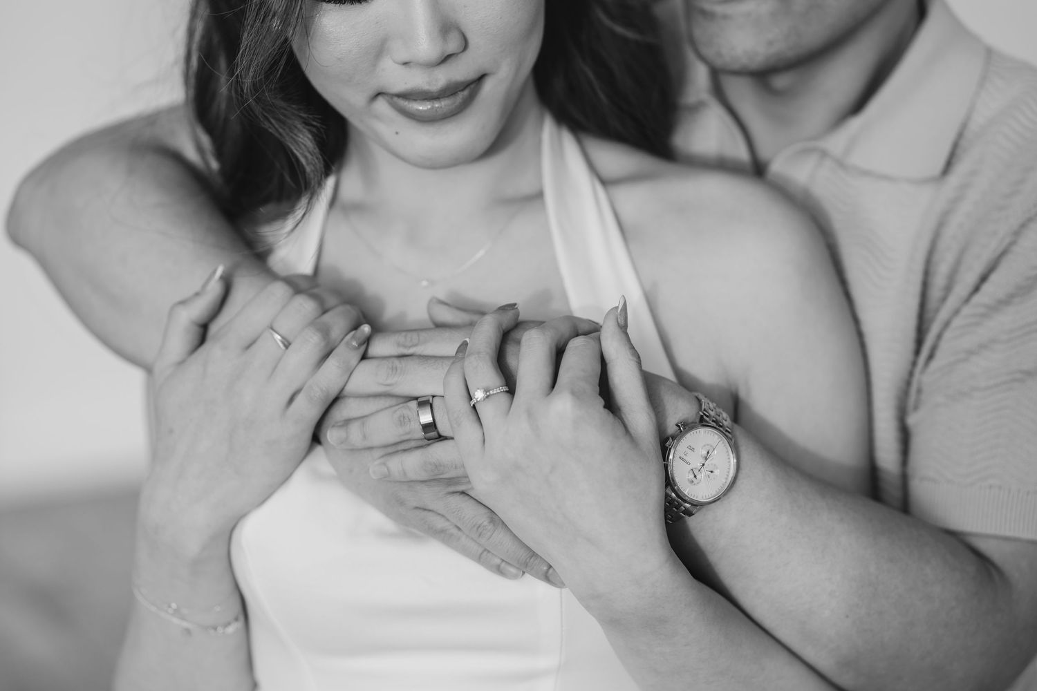 Black and white close-up photo showing hands embracing with engagement ring and wristwatch visible.