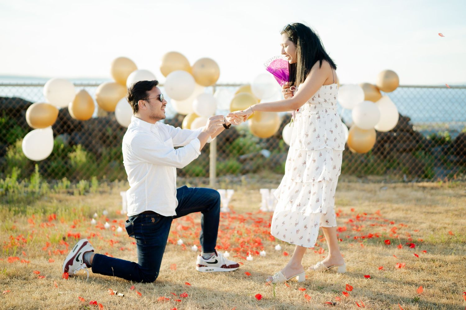 The moment just before the question, balloons and petals behind them, West Point Lighthouse proposal photographer, Seattle