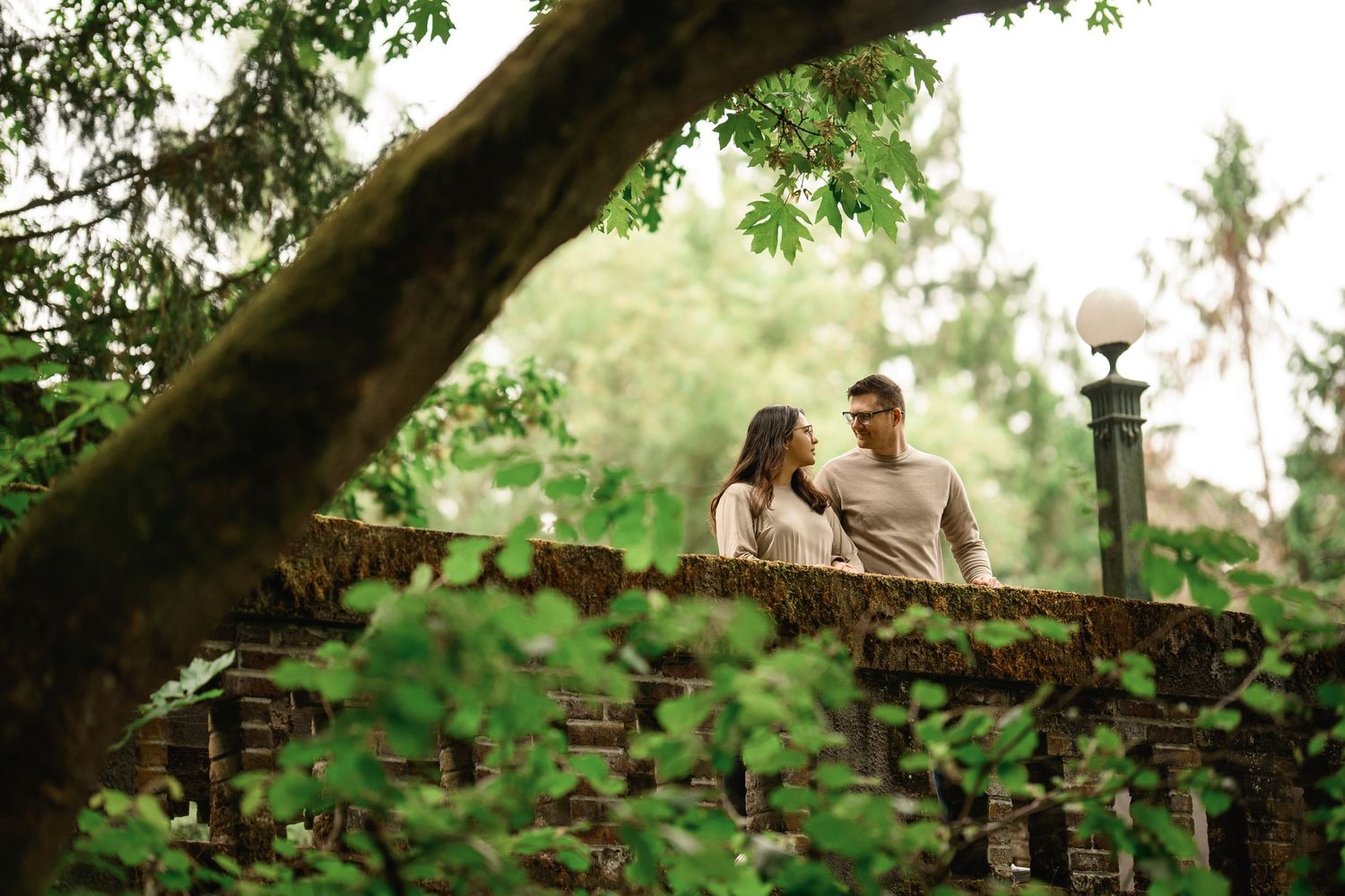 Couple on the Wilcox Footbridge seen through overhanging branches, Washington Park Arboretum proposal photographer, Seattle