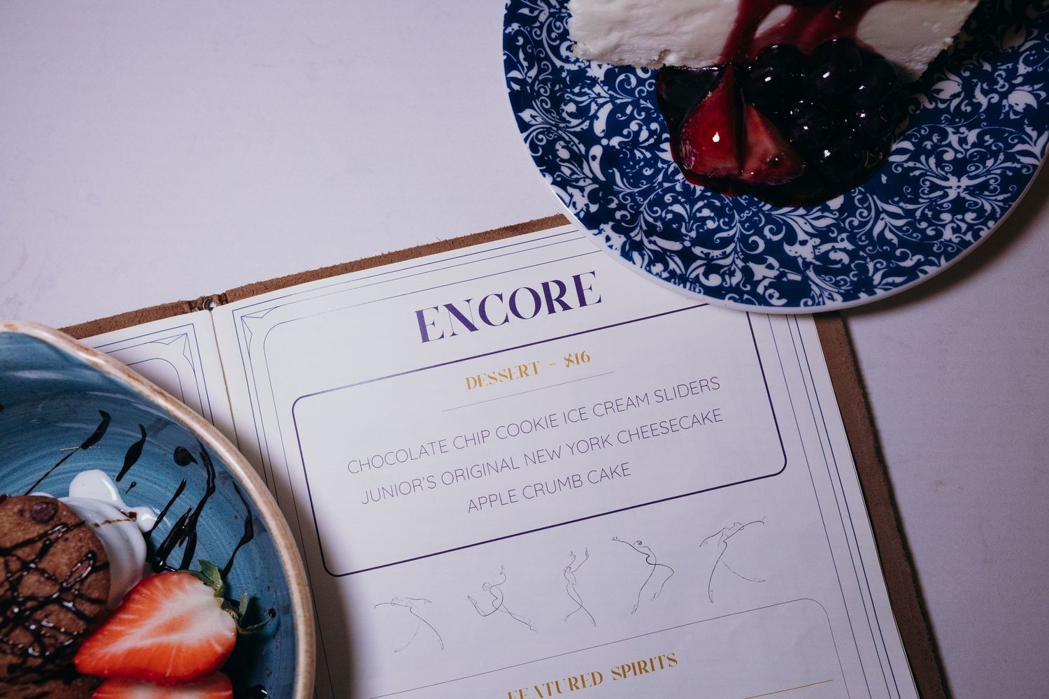An 'Encore' menu card sits on a table next to blue plates with fresh strawberries and desserts.