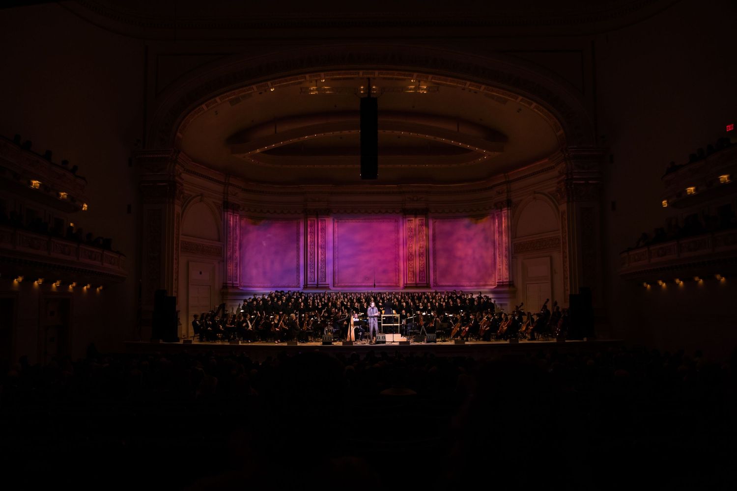 Concert hall stage with performers under dramatic red lighting and ornate backdrop.