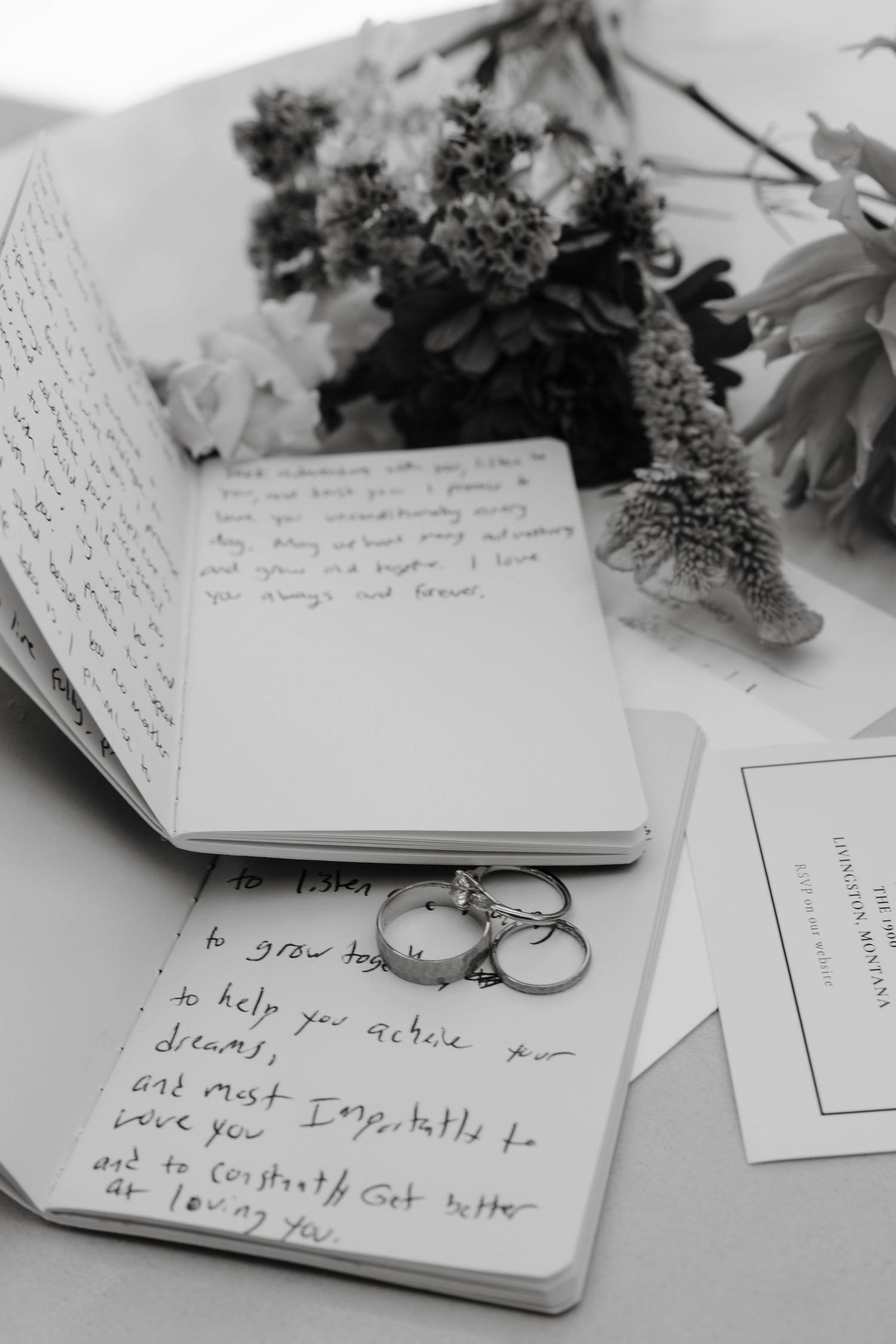 Black and white photo of wedding rings and handwritten vows with flowers.