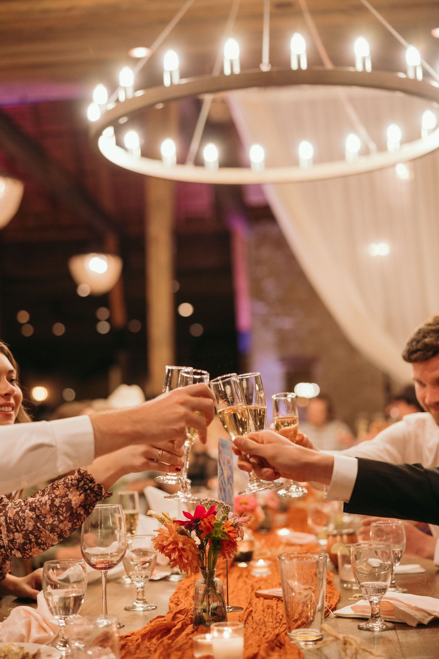 Elegant wedding reception table with candlelight, floral centerpieces and raised champagne glasses.