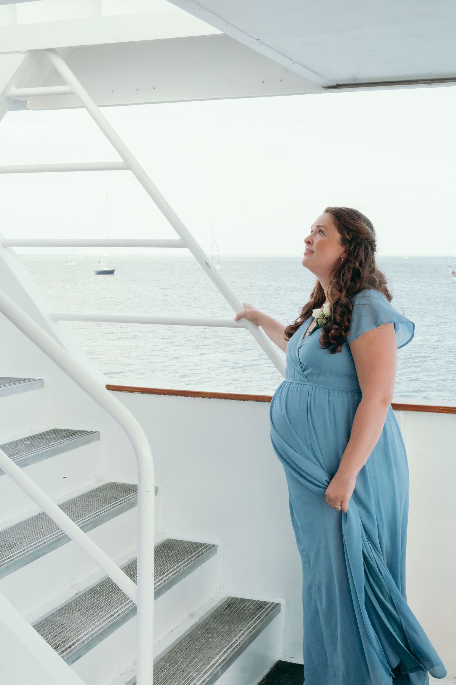 Person in a blue dress twirling on a white boat deck with water views.