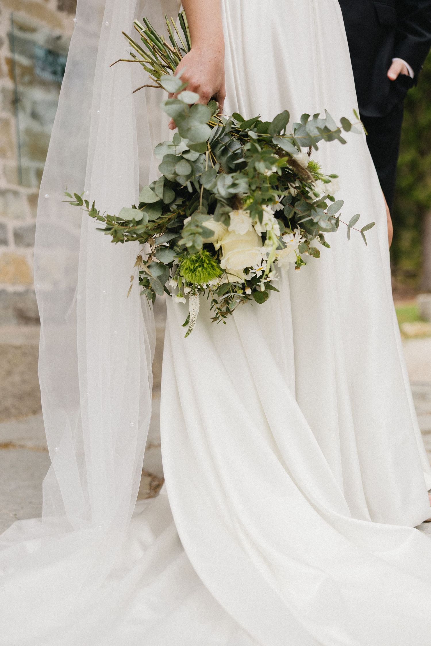 Elegant white wedding dress with flowing train and greenery bouquet details.