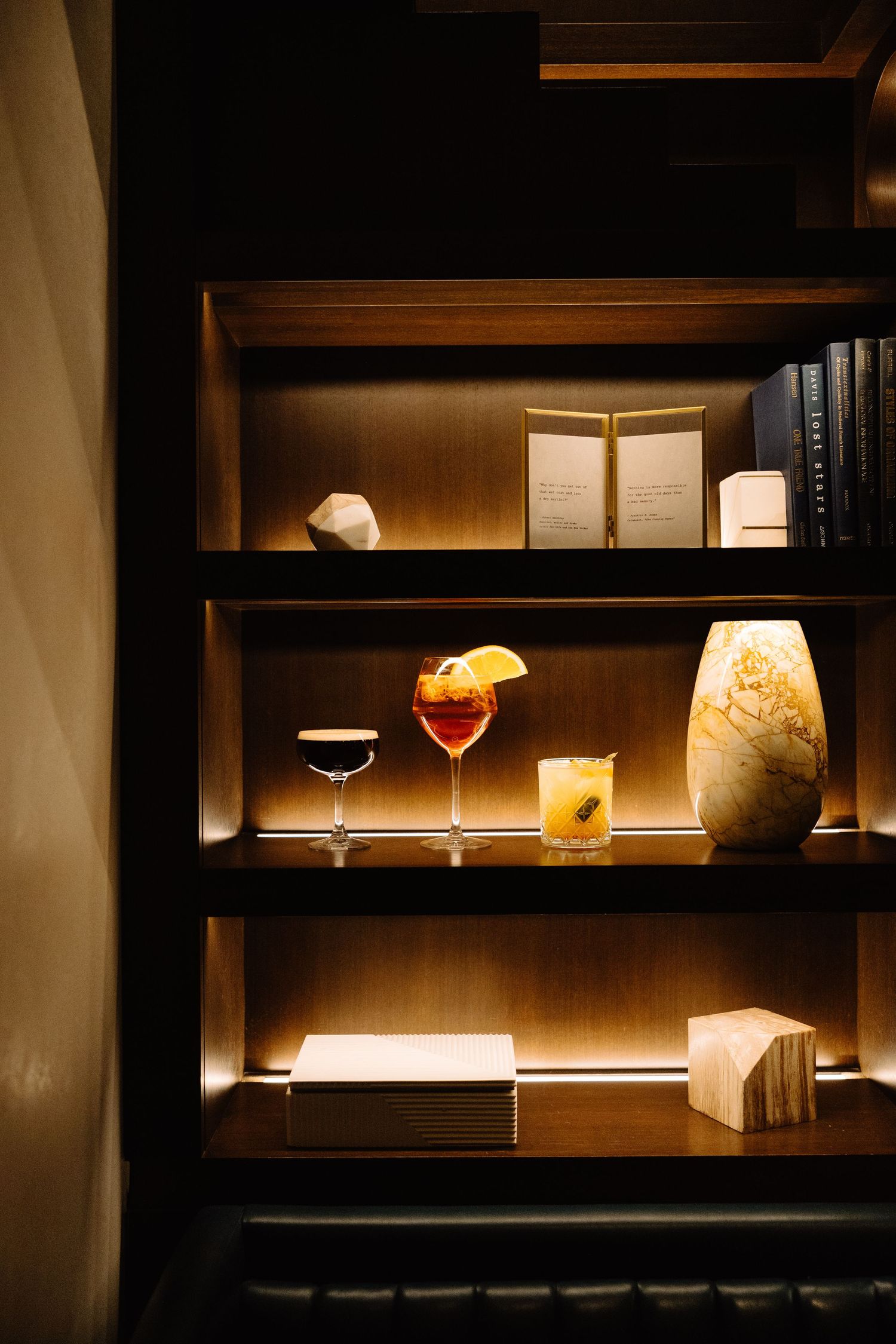 Dimly lit wooden shelves with illuminated glassware and books create a cozy bar or study atmosphere.