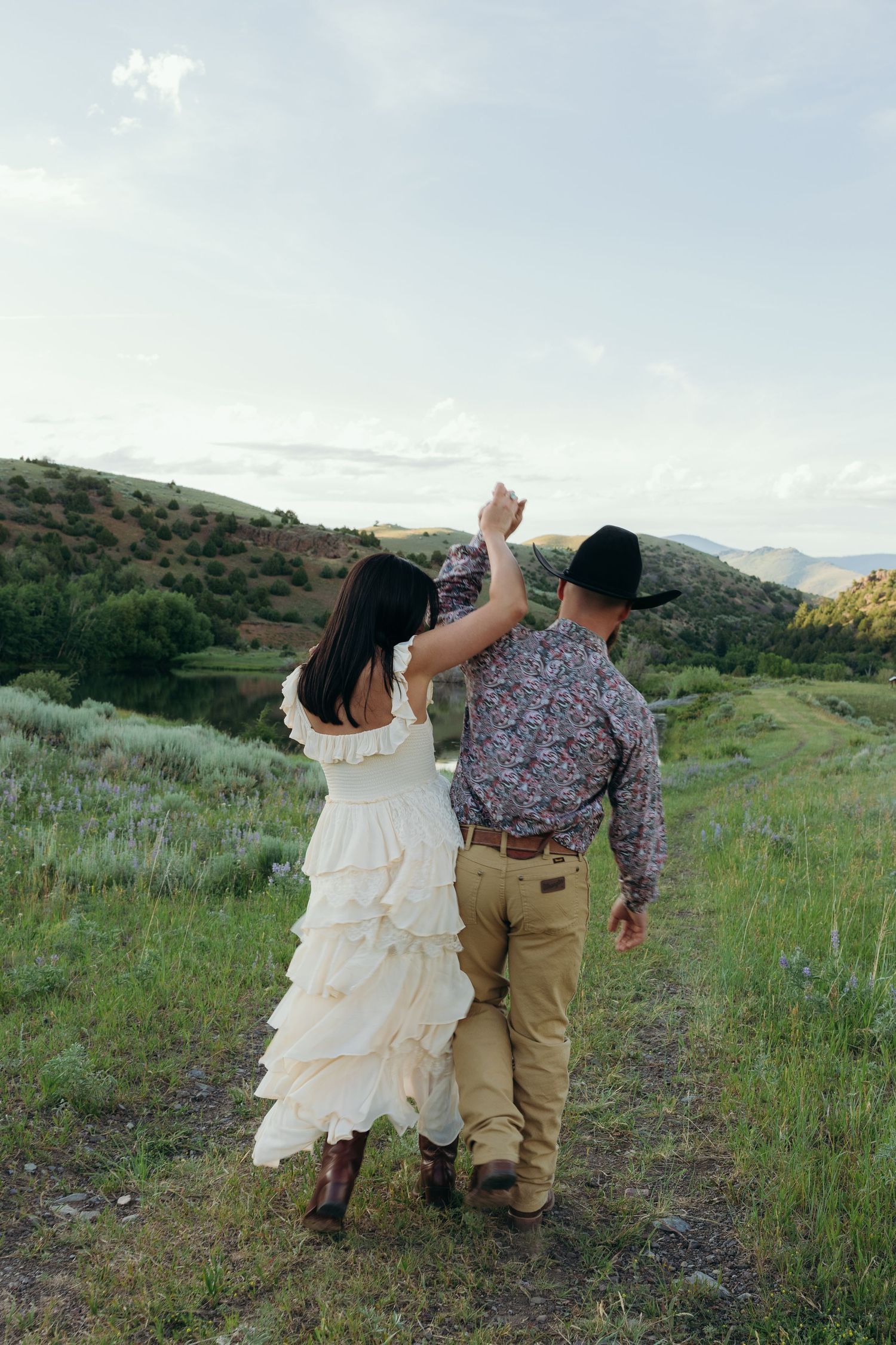 A playful couple dances together on a mountain trail during their photoshoot.